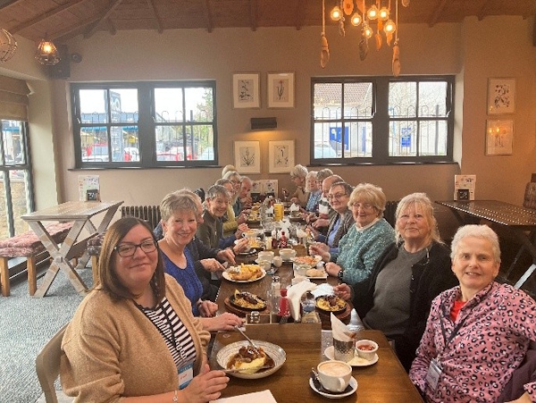 A group of people smile for the camera while sat around a table having a meal
